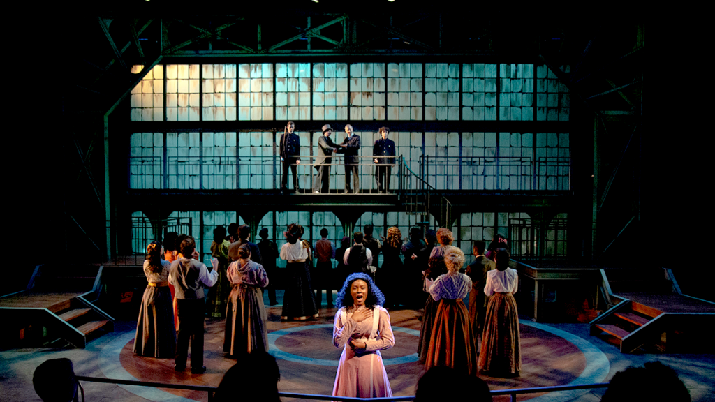 Ragtime the musical, singer is surrounded by dancers on a dark stage