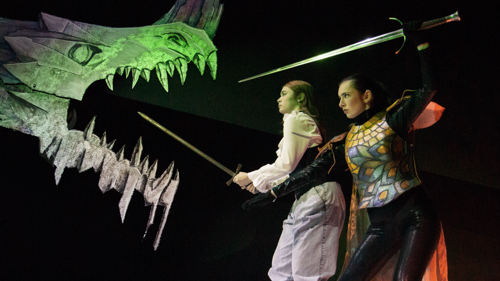 In this publicity image for University Theatre's production of "She Kills Monsters," Tilly Evans (Tilius The Paladin) and her sister Agnes, with swords drawn, face off with a Dungeons & Dragons-like dragon bearing its teeth.