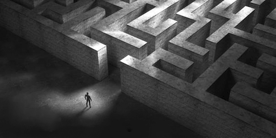 A maze constructed from concrete with a silhouetted man standing outside of the entrance about to enter.