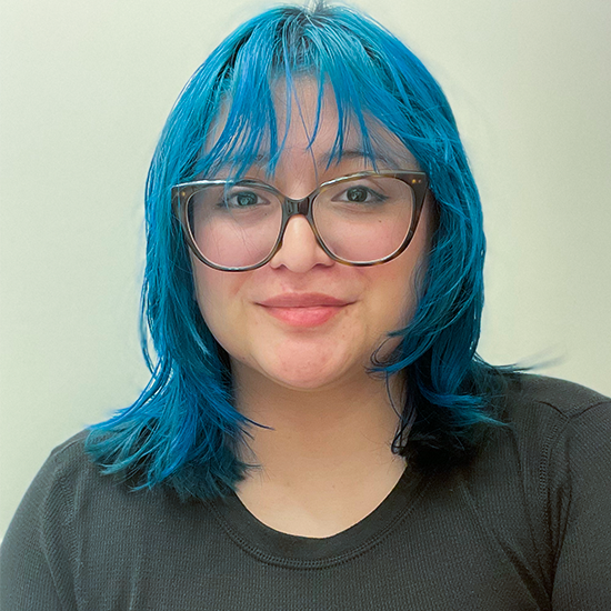 Quinn Froning sits for a portrait with aqua hair and a dark gray shirt.