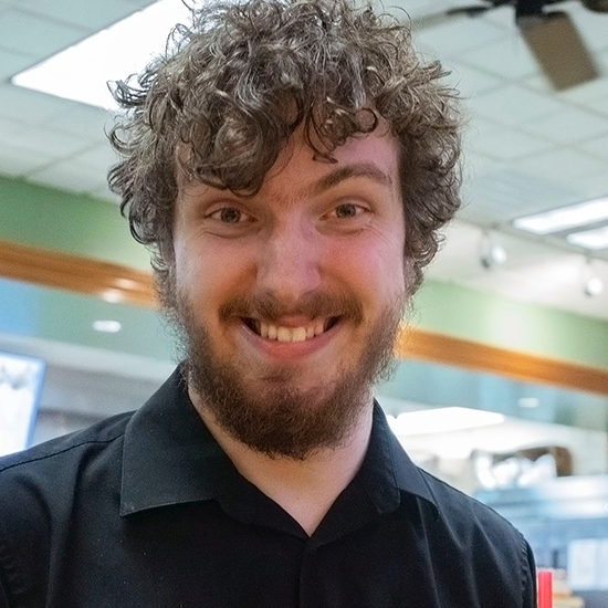 Coleman Hines, in a black collard shirt, looks into the camera.