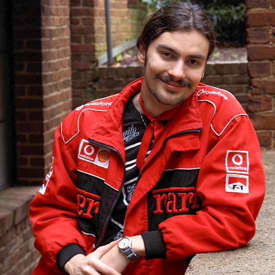 Micha Jones in a red, black and white jacket, leans on a brick railing surrounded by brick walls.