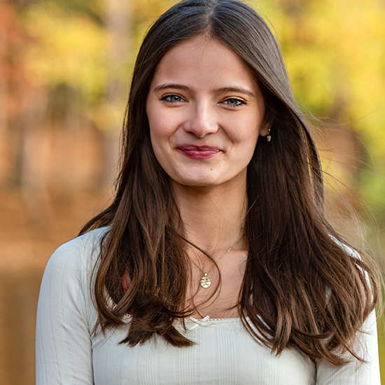Lilly Kindsvatter in a portrait wearing a white top in front of yellow foliage in the background.