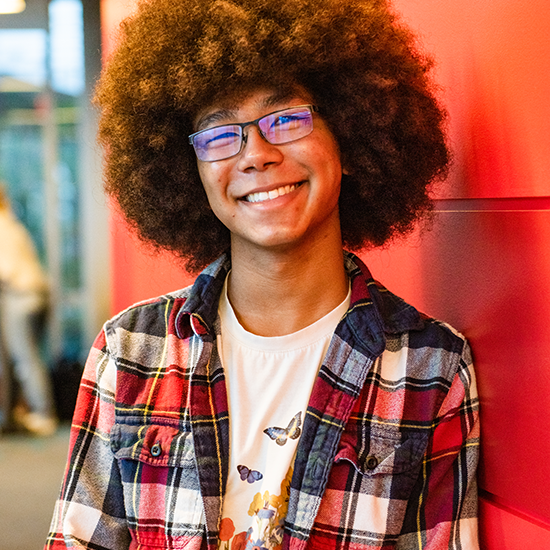 Brandon Leach, sporting a big afro, leans against a red wall.