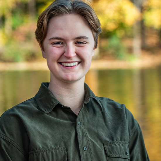 Dae Perry Reed, in a green top, sits by a body of water with yellow foliage on the banks.