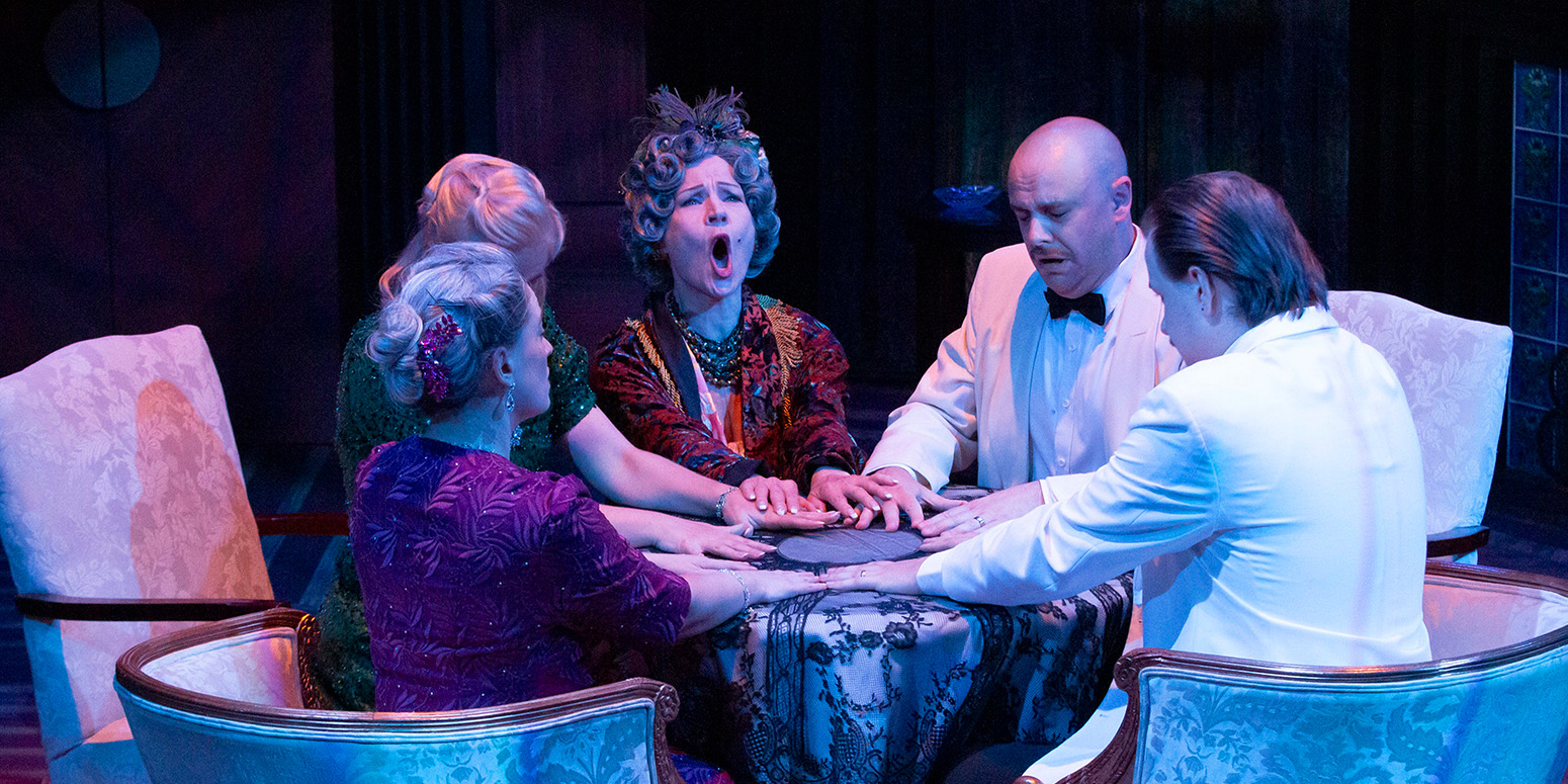 three women and two men sitting around with hands flat a table in a seance
